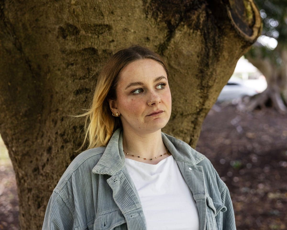 Shannon Stokes stand in front of a tree trunk, looking off to the side