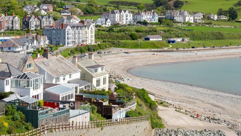 General view of the seaside town of Criccieth in north Wales, including a pebble beach and large townhouses overlooking the seafront, in the sunshine.