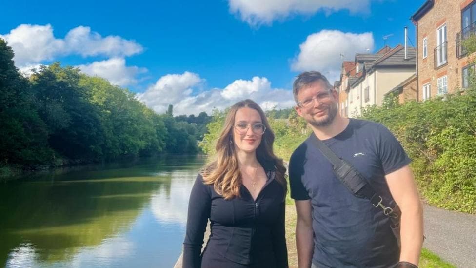 Nicola Irvine and Toby White stood by the River Avon with trees and houeses visible in the background.