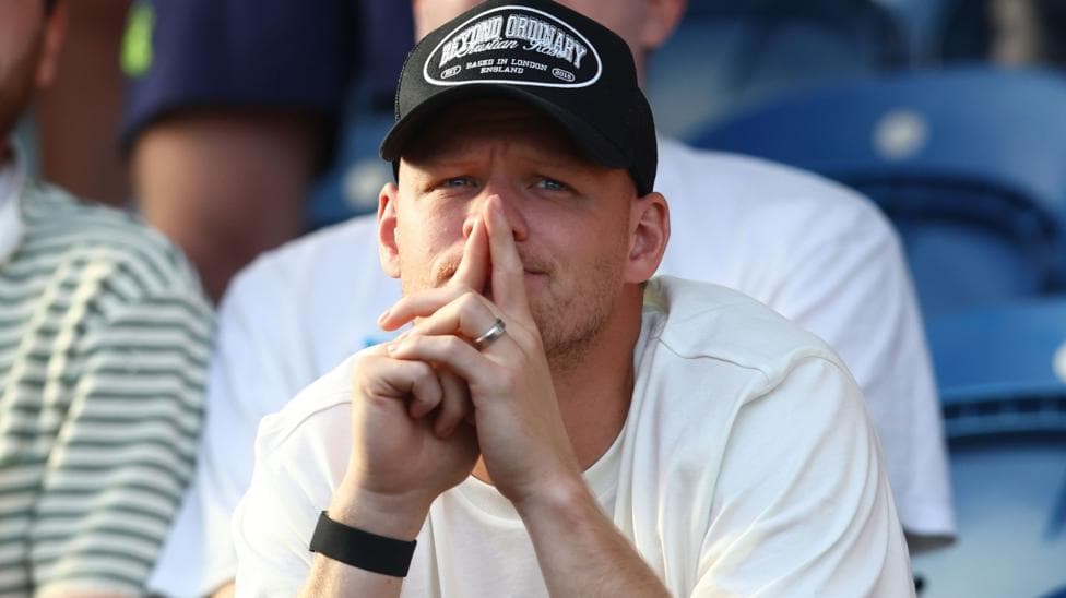 Aaron Ramsdale, wearing a black baseball cap and white t-shirt, watches Southampton's EFL Cup game at Colchester United from the stands