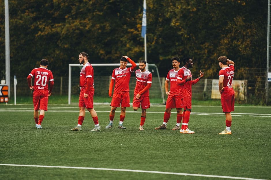 Amateur soccer team in red uniforms gathering on a green field during daytime.