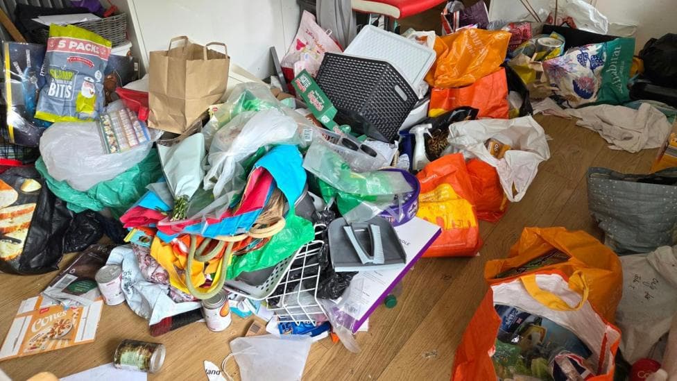 Plastic bags, objects, packaging and more items almost fully cover an area of wooden floor.