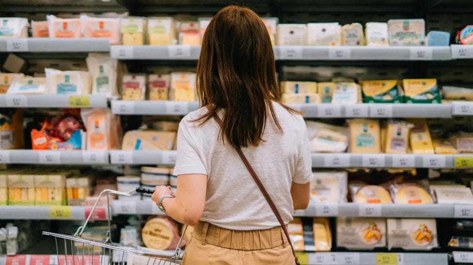 A woman from behind holding a shopping basket while looking at the cheeses on offer in a supermarket