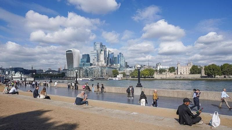 People sit in the autumn sunshine by the London Riverside in London