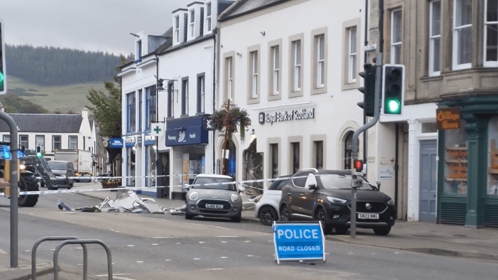 A taped-off Royal Bank of Scotland branch with windows smashed and debris outside. There is a police road closed sign outside it.
