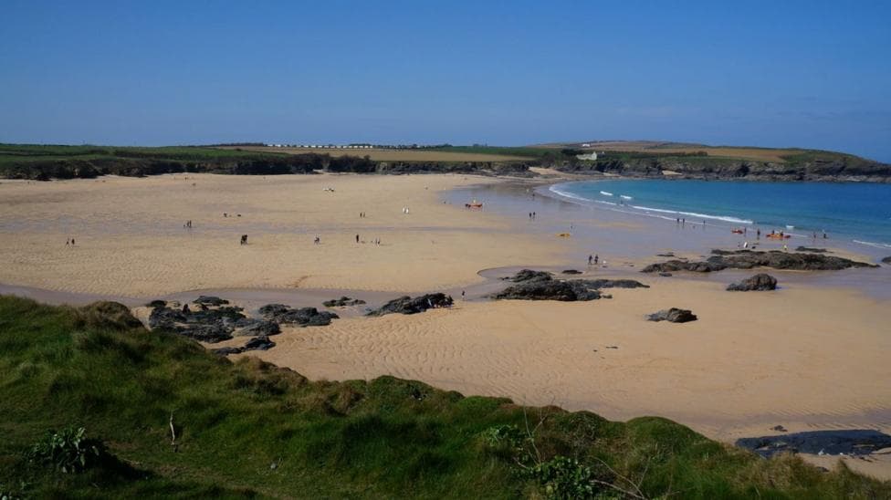 The image shows a wide sandy beach. There is a number of rocks within the sand and cliff faces surrounding the beach.