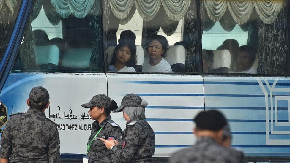 People look out the window of a bus while personnel in military uniform stand in the foreground