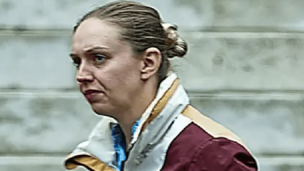 Photo of police officer, Fiona Anderson. Her blonde hair is tied up in a bun and she is not smiling. She wears a white and maroon raincoat.