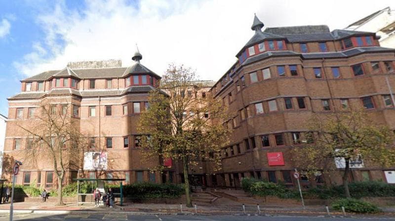 Cardiff Sixth Form College is a red brick building with trees, a road and a bus stop outside. It is several storeys high, and has a red sign on it.