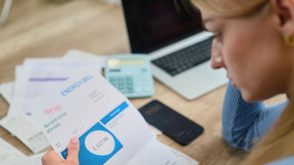Woman looks at energy bill with paperwork, a calculator and a laptop on the table in front of her.