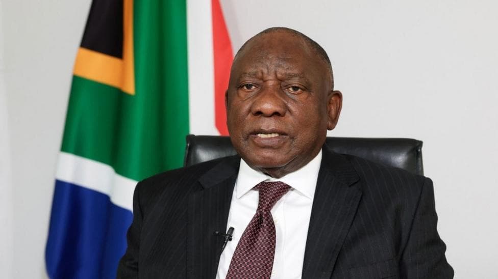 President Cyril Ramaphosa in a suit and tie with the South African flag seen behind him