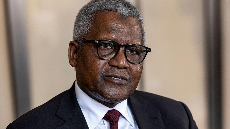 A man dressed in black suit, white shirt and maroon tie. He is wearing black spectacles frames as he stares into the camera.