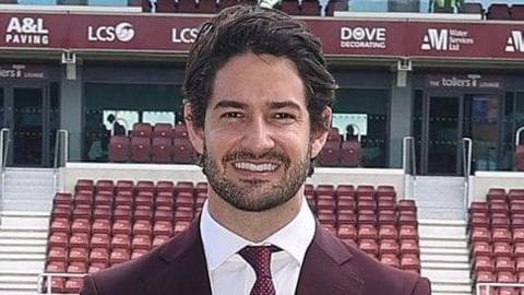 Alexandre Pato standing by side of Sixfields pitch, wearing maroon suit, white shirt, red tie and cream shoes, smiling with hands in pockets.