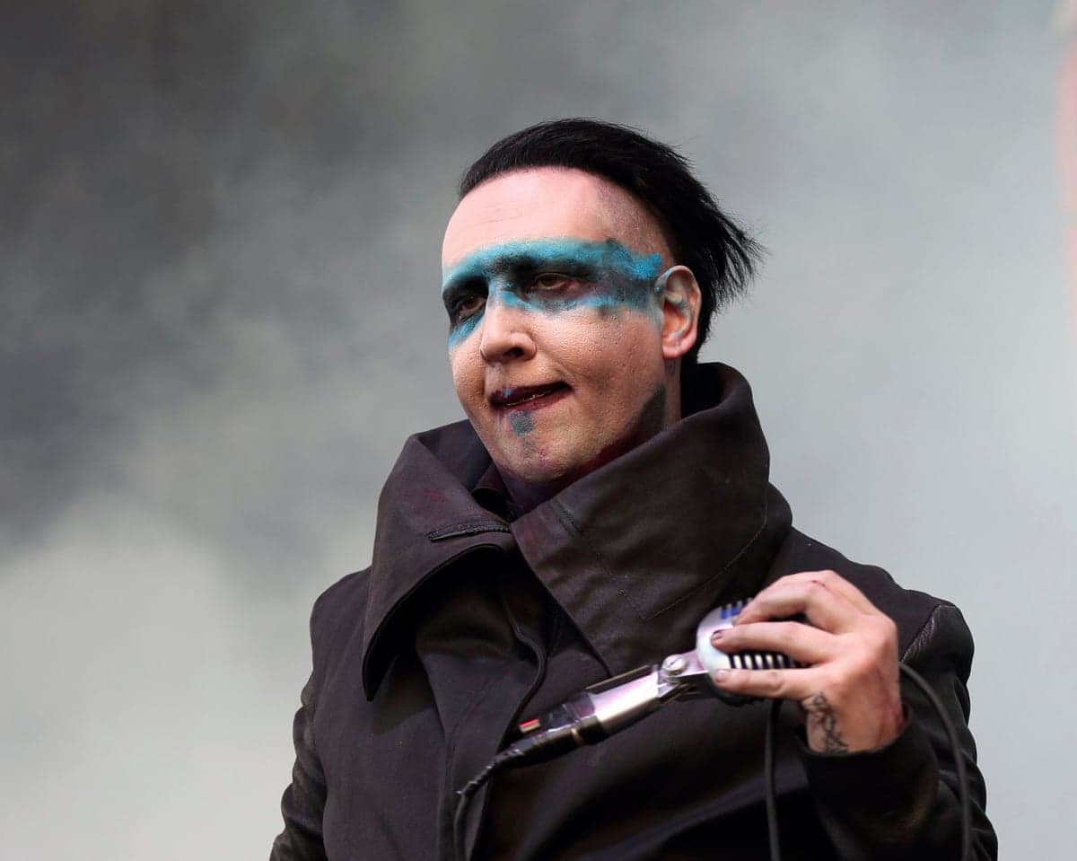 Marilyn Manson, with blue eye makeup, holds a microphone while performing onstage
