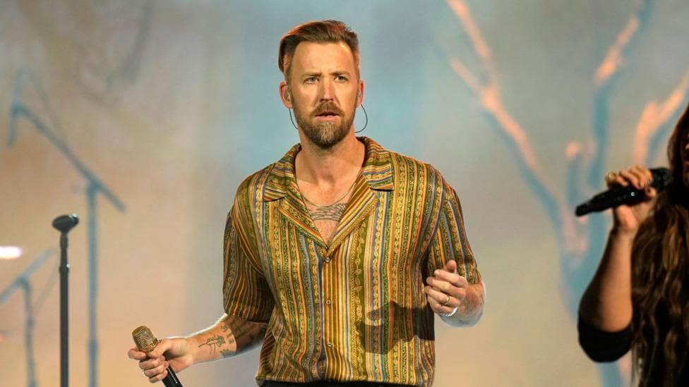 Charles Kelley of Lady A performing onstage during the 2024 People's Choice Country Awards at Grand Ole Opry House in Nashville, Tennessee. He is wearing a gold stripey shirt and holding a microphone.