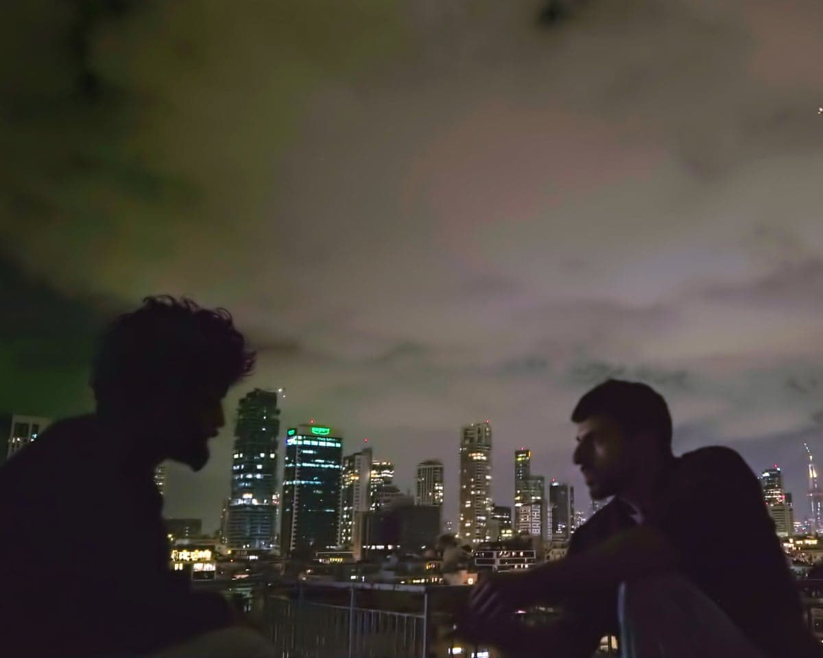 In a scene from NAZA, a man's silhouette is seen in profile against a night-time city skyline with illuminated skyscrapers