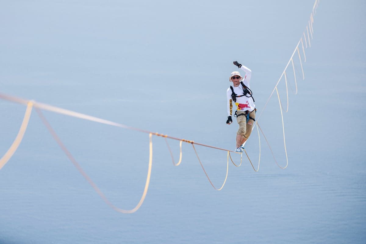 Jaan Roose balances on a highline rope high above the sea, raising his fist and smiling