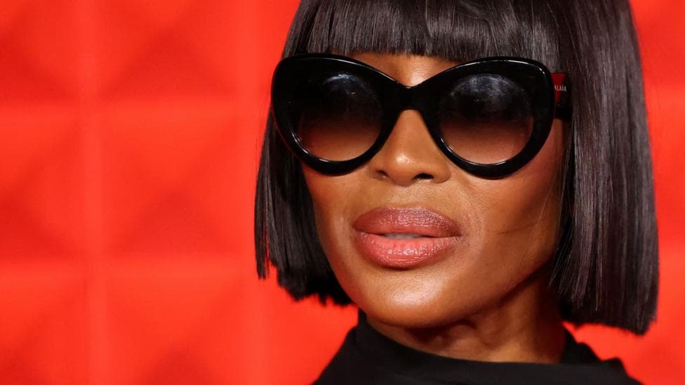 Naomi Campbell wearing dark glasses against a red background