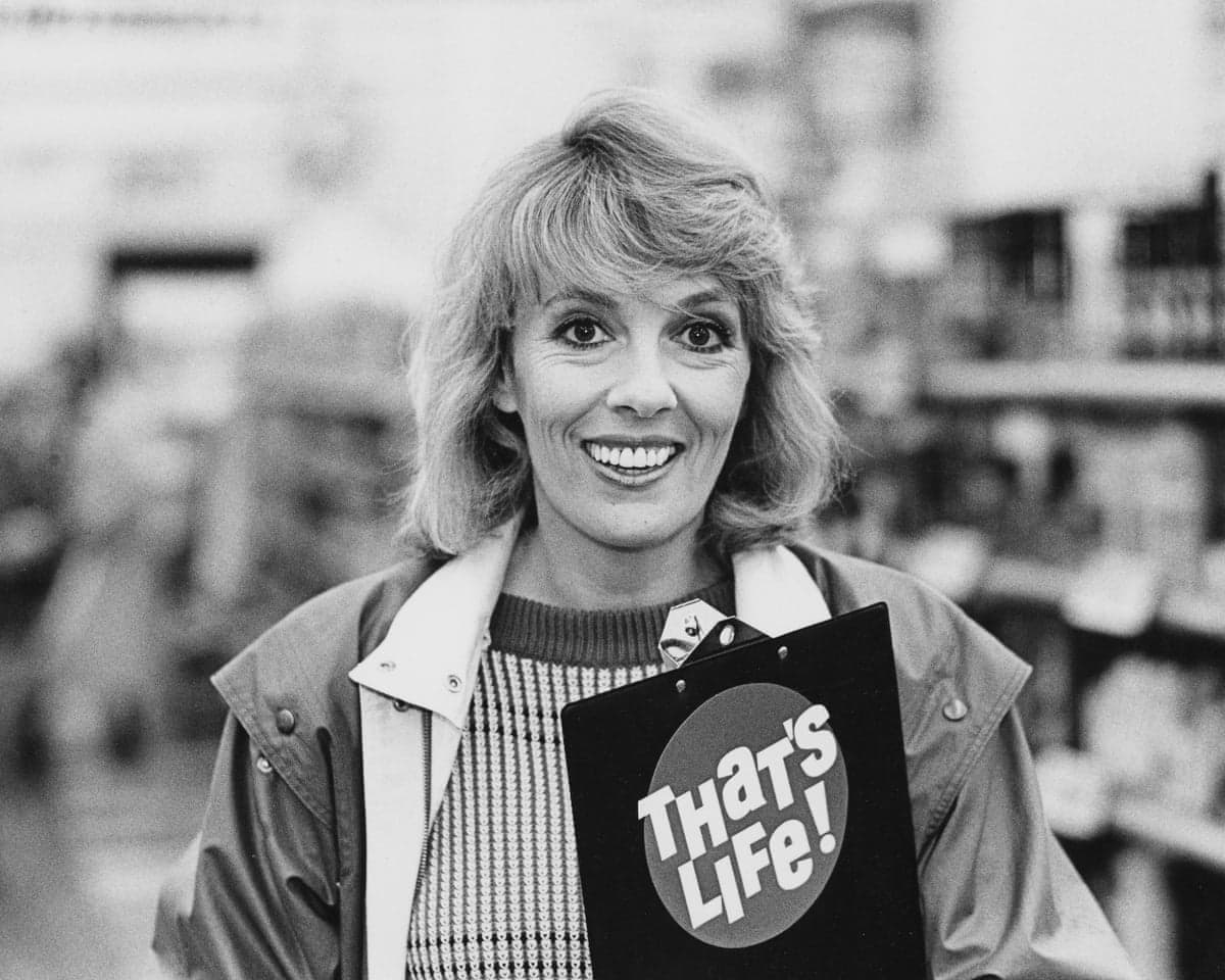 Esther Rantzen smiles holding a "That's Life!" clipboard