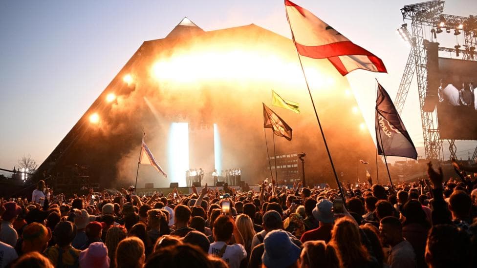 A crowd is standing in front of a stage during sunset.