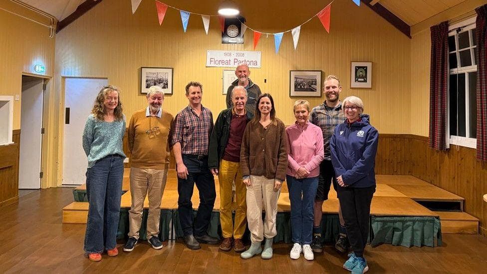 A group of villagers in a village hall with bunting above their heads smiling in celebration