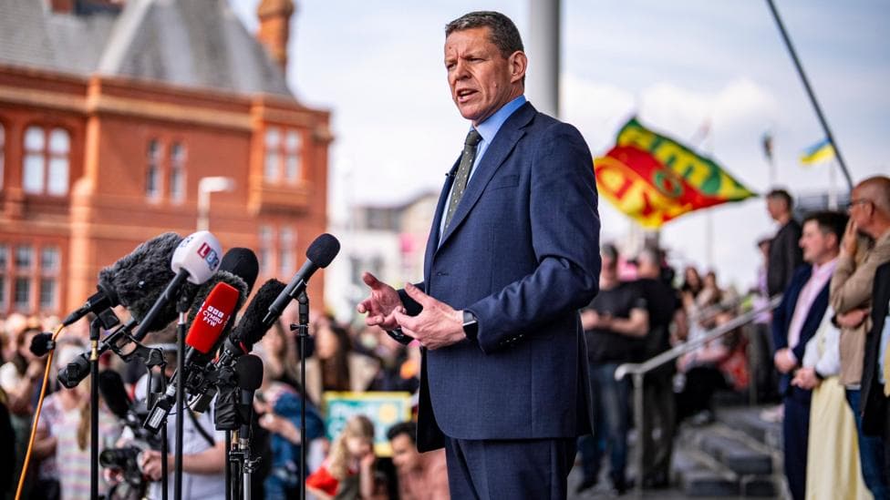The image shows Rhun ap Iorwerth addressing a crowd outside the Senedd following May's Senedd election result.