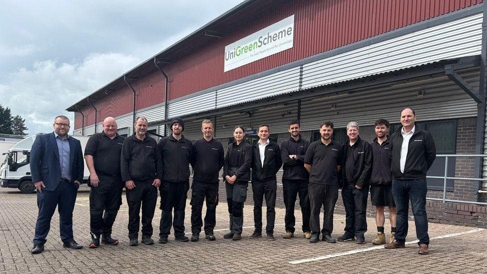 A group of workers outside a factory with a sign saying UniGreenScheme above their heads