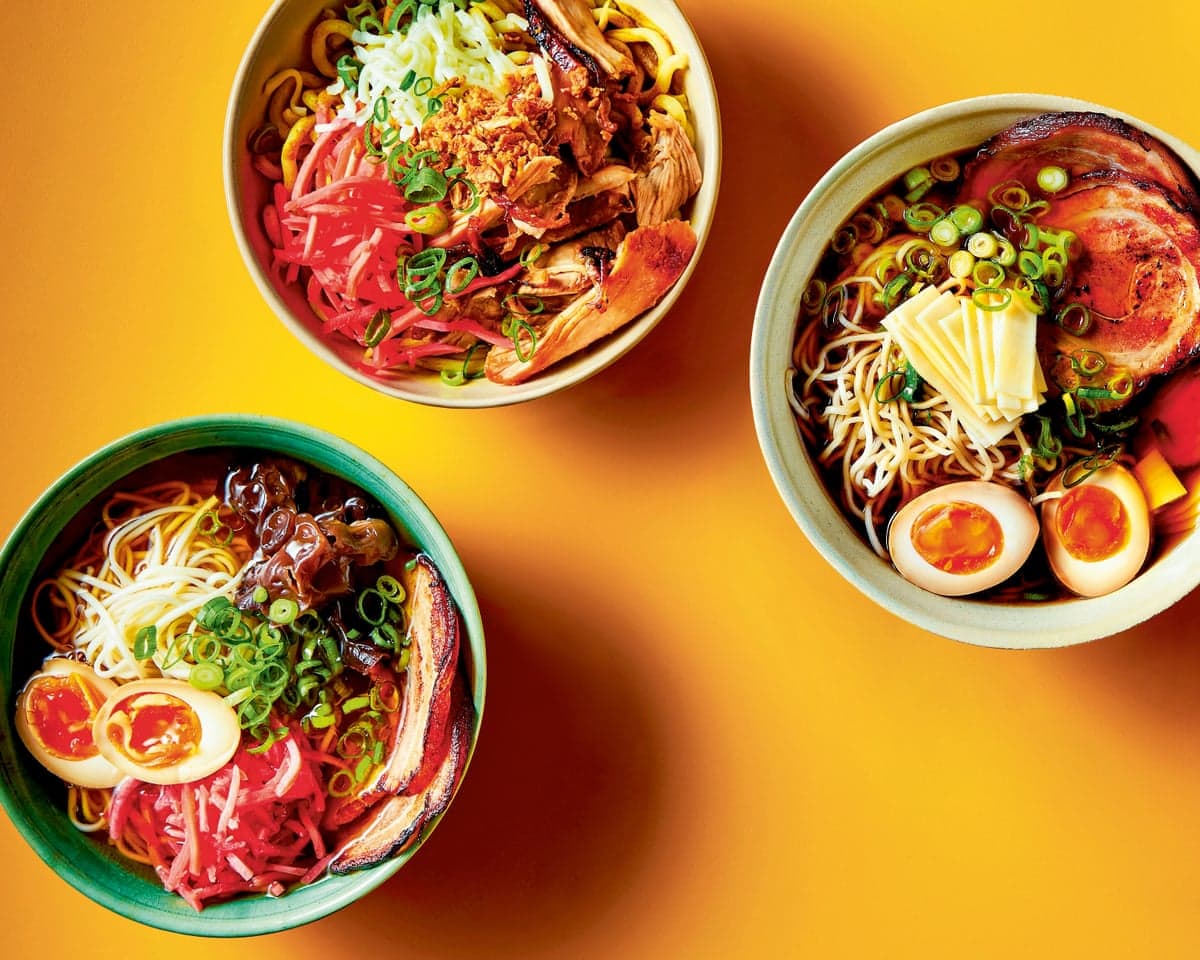 Five bowls of ramen with noodles, eggs, meat, and vegetables sit on a yellow surface