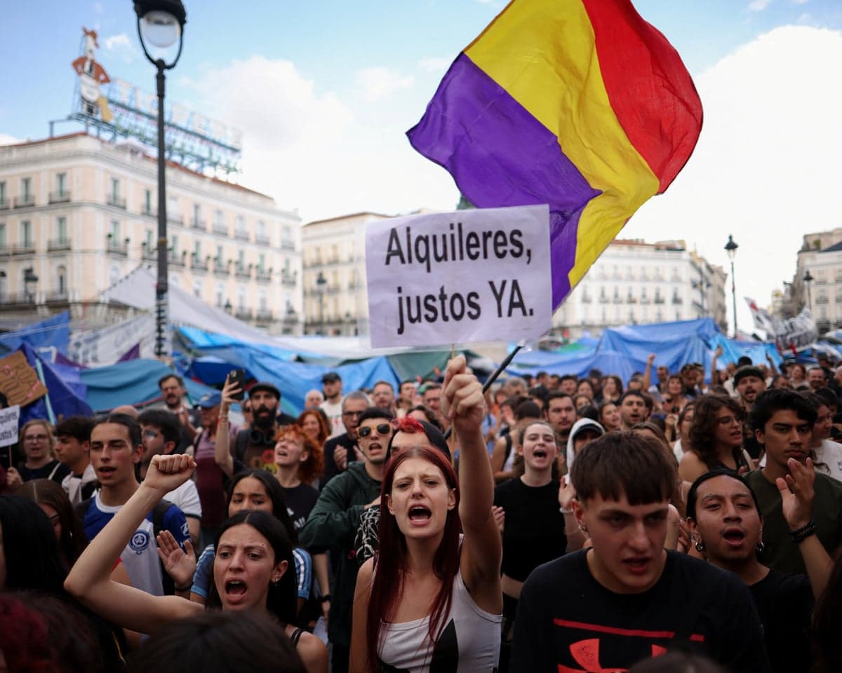 A crowd of mostly young protesters waving banners and flags in front of a sea of tents set up as a protest camp