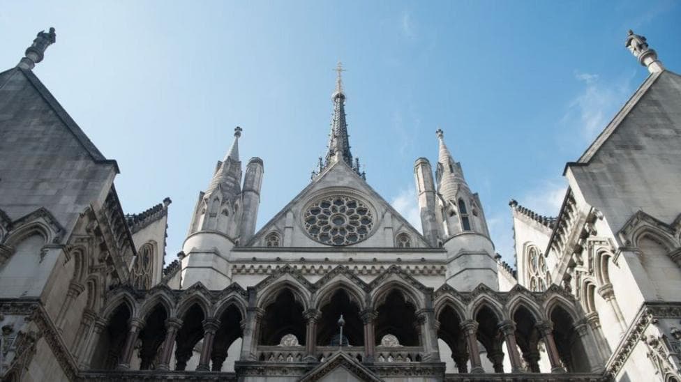 A low view of the Royal Court of Justice in London, the sky above it is blue and the sun is shining.