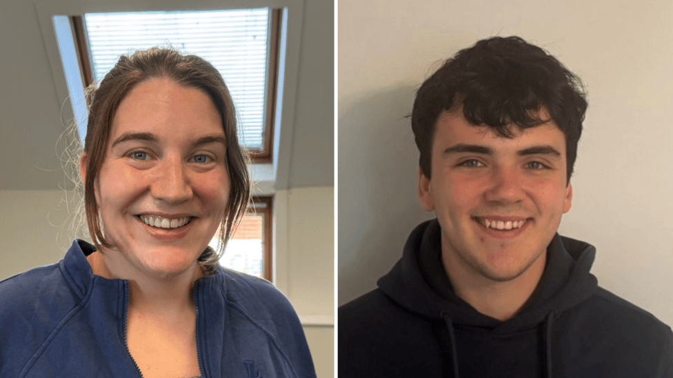 Two people. On the left, a woman with brown hair smiling at the camera. She is wearing a blue fleece. The walls behind her are white, and there is a sky-light. On the right, a man with black hair smiles at the camera. He is wearing a black hoodie and standing in front of a plain white wall.