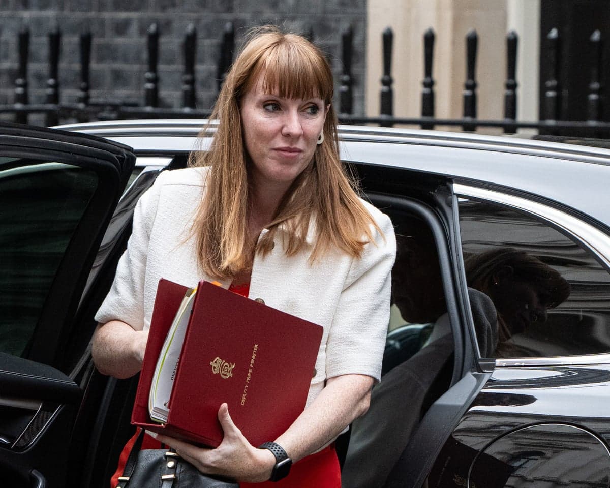Angela Rayner holding a red folder steps out of black car.