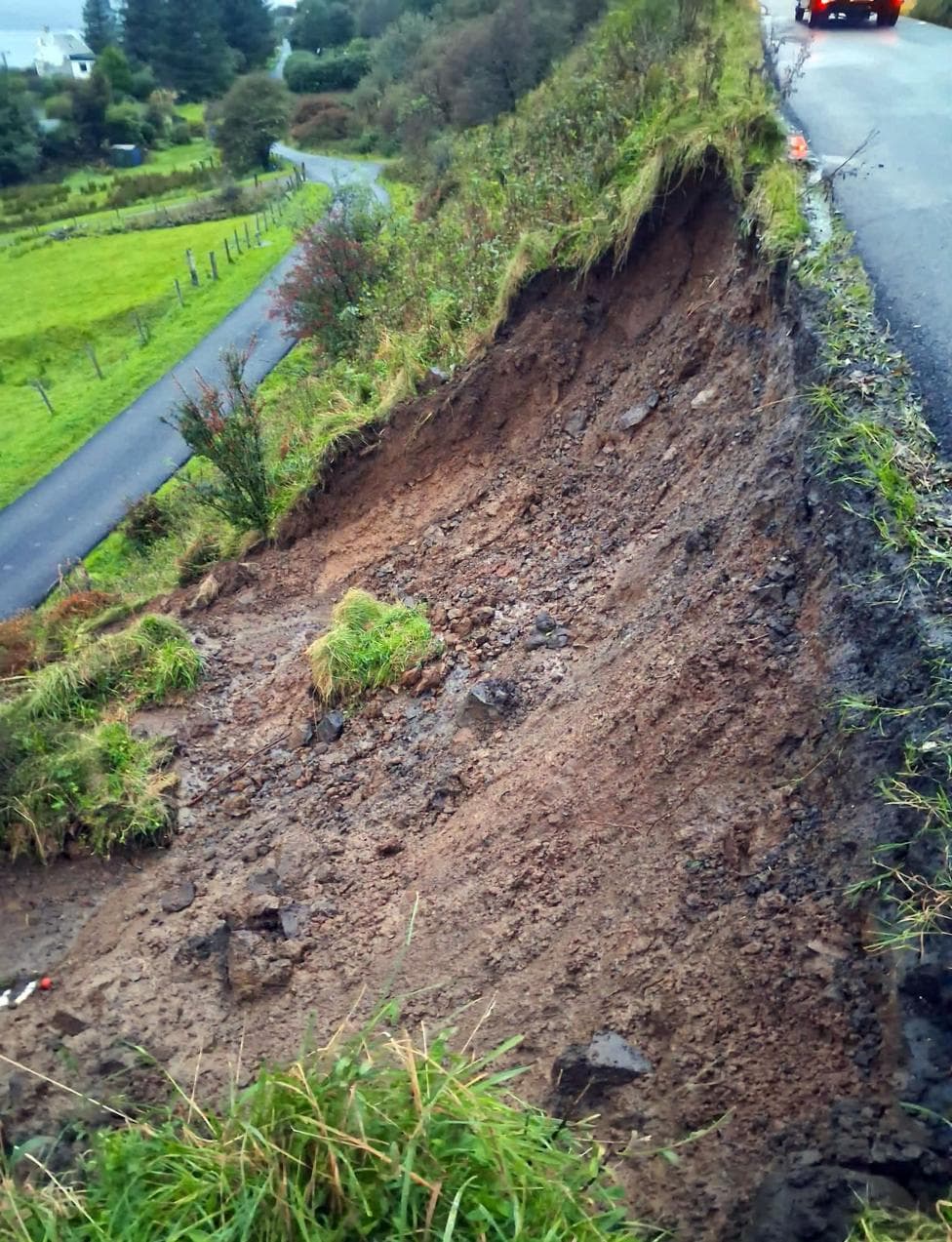 A bare area of soil after a landslip from the side of a higher road onto a smaller road below