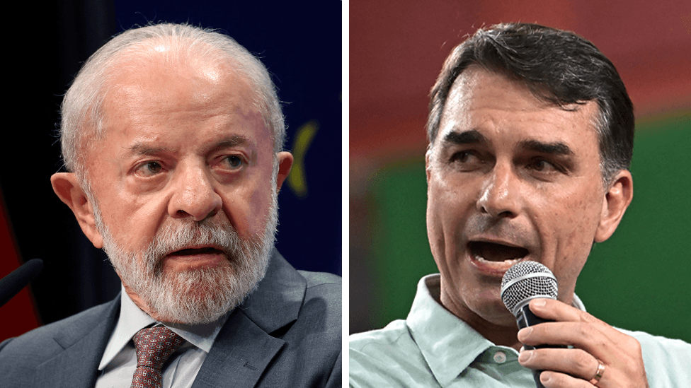A composite image shows Luíz Inácio Lula da Silva, wearing a grey suit jacket and a burgundy tie, at the left, and Flávio Bolsonaro, wearing a light green shirt but no tie, speaking into a microphone.