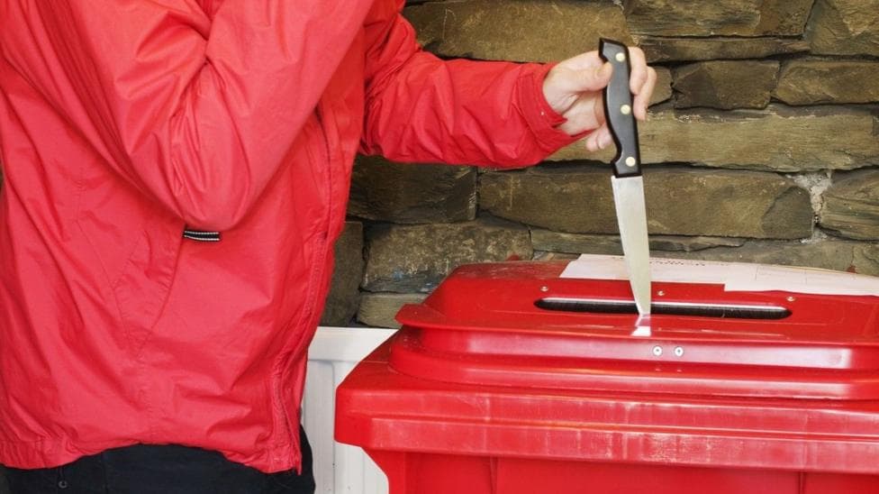 A person in a red coat places a silver knife with a black handle in a red bin, which has a hole in the top of it.