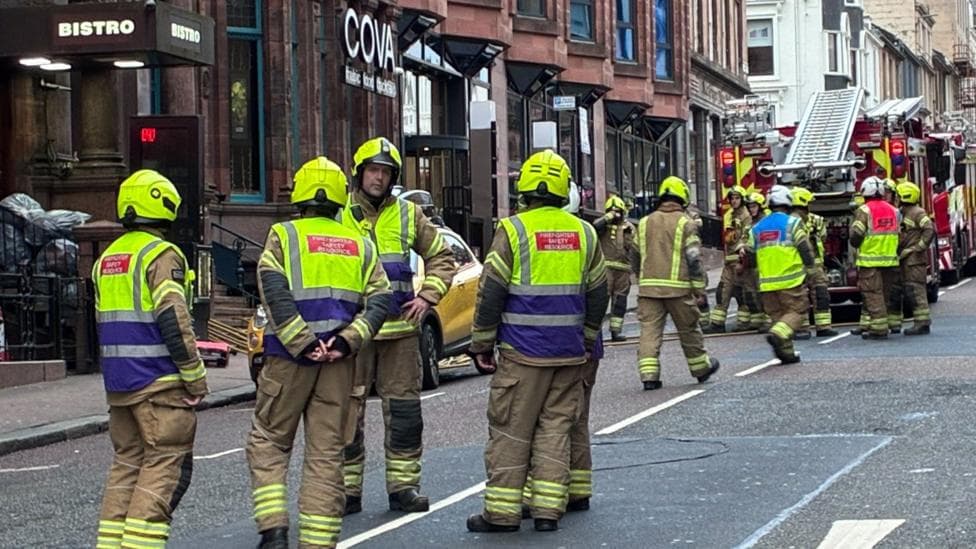 Firefighters gathered in a street with fire engines and a bar called Bistro in the background