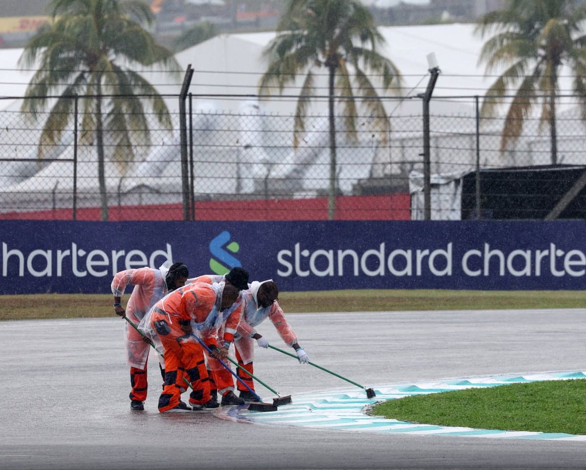 Track marshalls in rain gear sweep water off the racetrack with brooms
