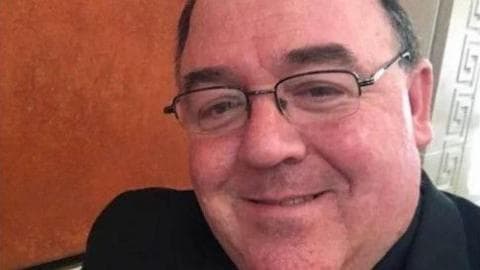 Fr Edward Gallagher.
He is wearing glasses and dark clothing, and smiling