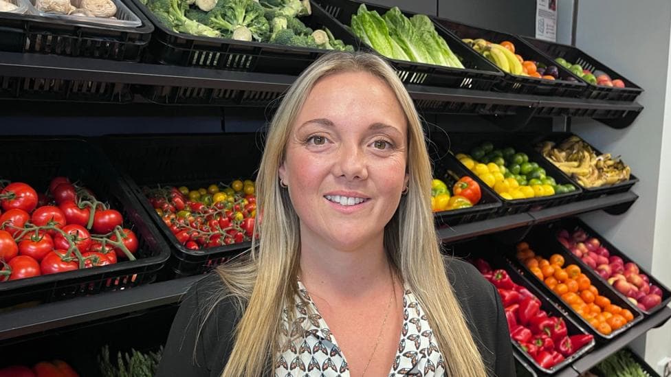 Gina English from the SEK Community Food Shop in Chatham standing behind a bright display of fruit and vegetables