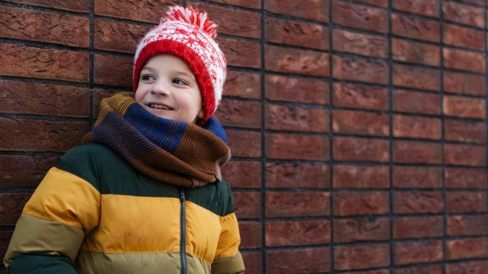 A child in a yellow puffer coat, scarf and red hat