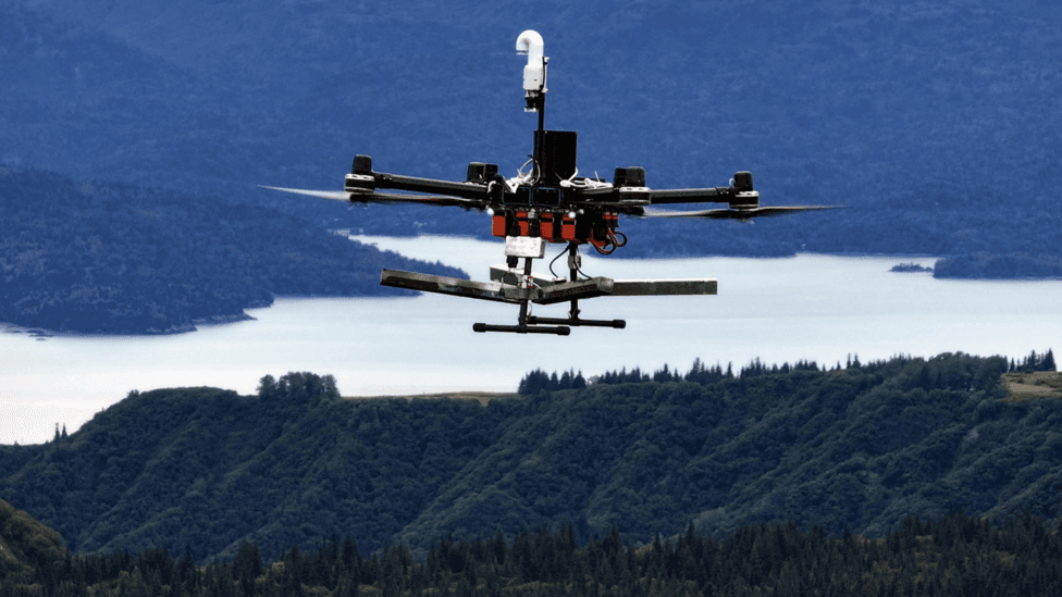 A Rainmaker drone flies over forests and a lake in Alaska.