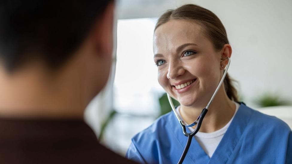 A female doctor wearing a stethoscope smiles at an unidentified patient
