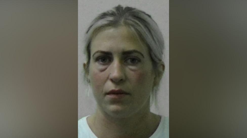Mugshot of Dronsfield. She has blonde hair tied behind her ears and appears to have bags under her eyes.