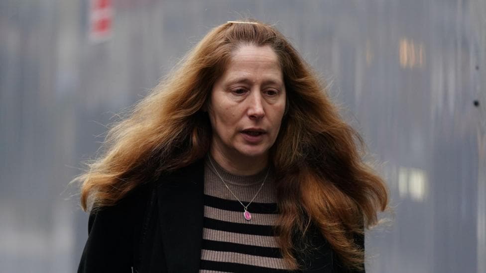 Isabel Vaughan-Spruce. A woman with long auburn hair, wearing a black jacket and stripey top and a necklace.