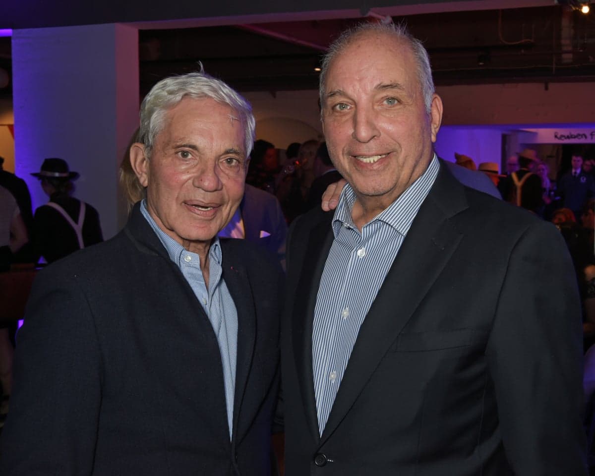 Simon and David Reuben attend an event at the Lyric Hammersmith theatre in 2015 to mark the opening of the theatre's Reuben Foundation wing. They are in their 70s in this picture and have grey hair; they both wear dark suits over open-necked light cotton shirts, David's striped.