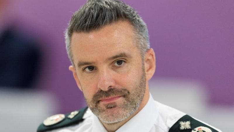 A man with grey and black hair and beard wearing a white police shirt with black lapels with symbols on them.