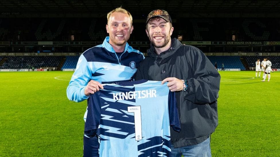 Two men holding a football top that says Kingfishr 1