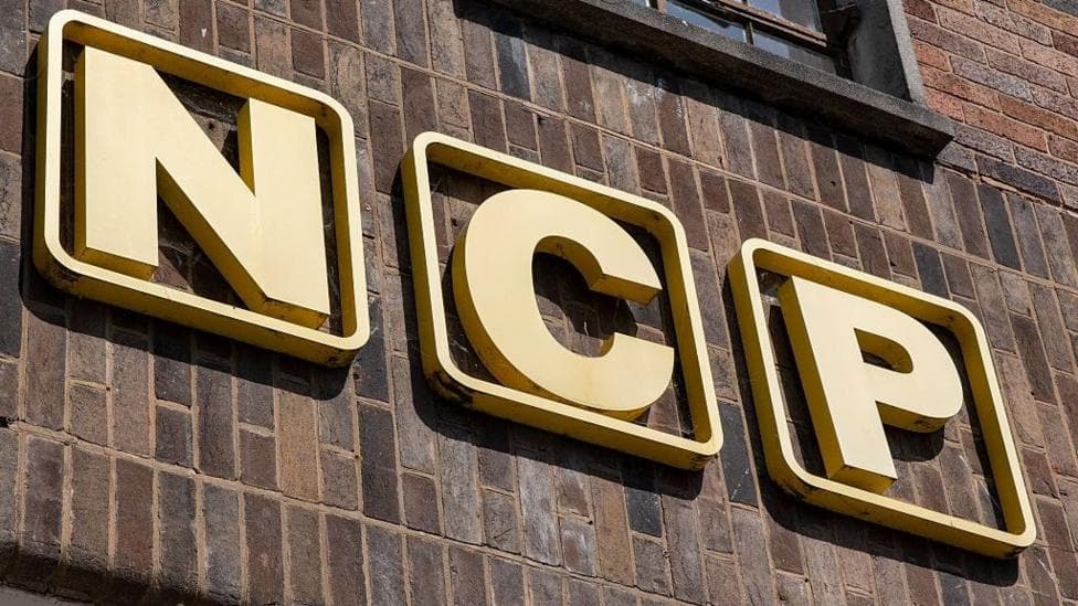 Yellow NCP sign on a brown brick wall.