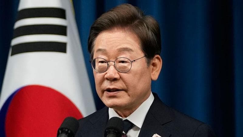 South Korean President Lee wearing a suit and speaking in front of a microphone