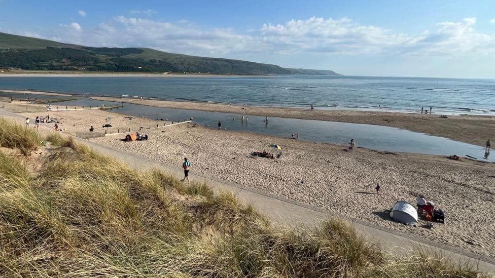A general view of Barmouth beach. Sand dunes with grass on top can be seen in the foreground, with a sandy beach and the sea beyond.